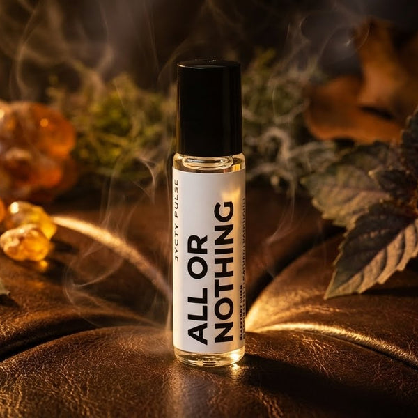 Small perfume oil bottle labeled 'All or Nothing' surrounded by amber stones and leaves on a dark background. Long lasting and vegan oil by JYCTY