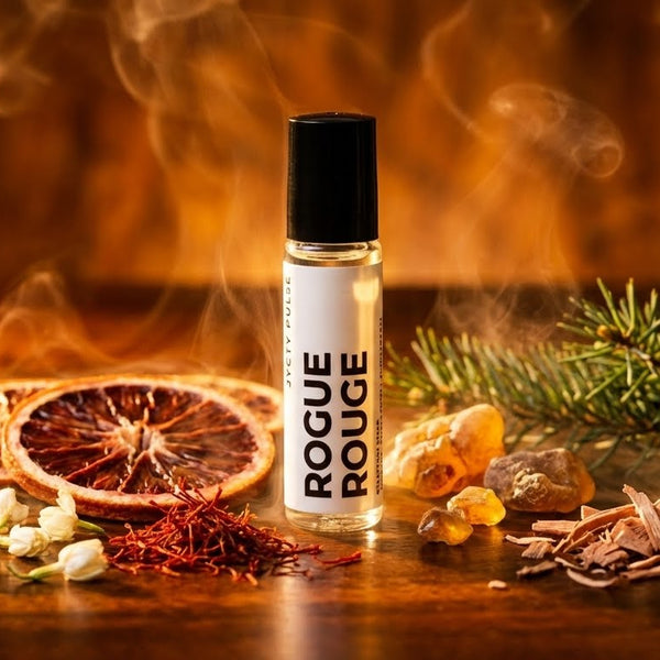 Roll-on bottle of 'Rogue Rouge' perfume oil on a wooden surface with dried fruits and flowers. Long lasting and vegan oil from JYCTY