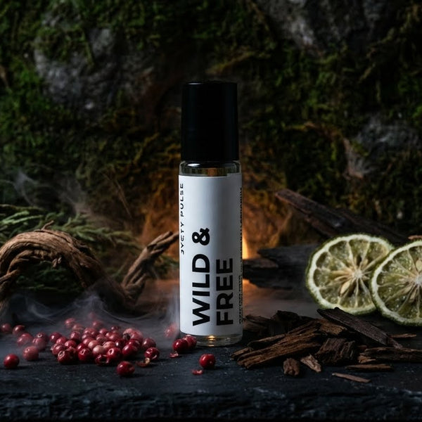 Perfume oil with 'Wild & Free' label on a dark surface with spices and herbs. long lasting and vegan perfume oil for men